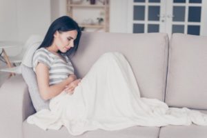 Woman sitting on a sofa holding her stomach in pain
